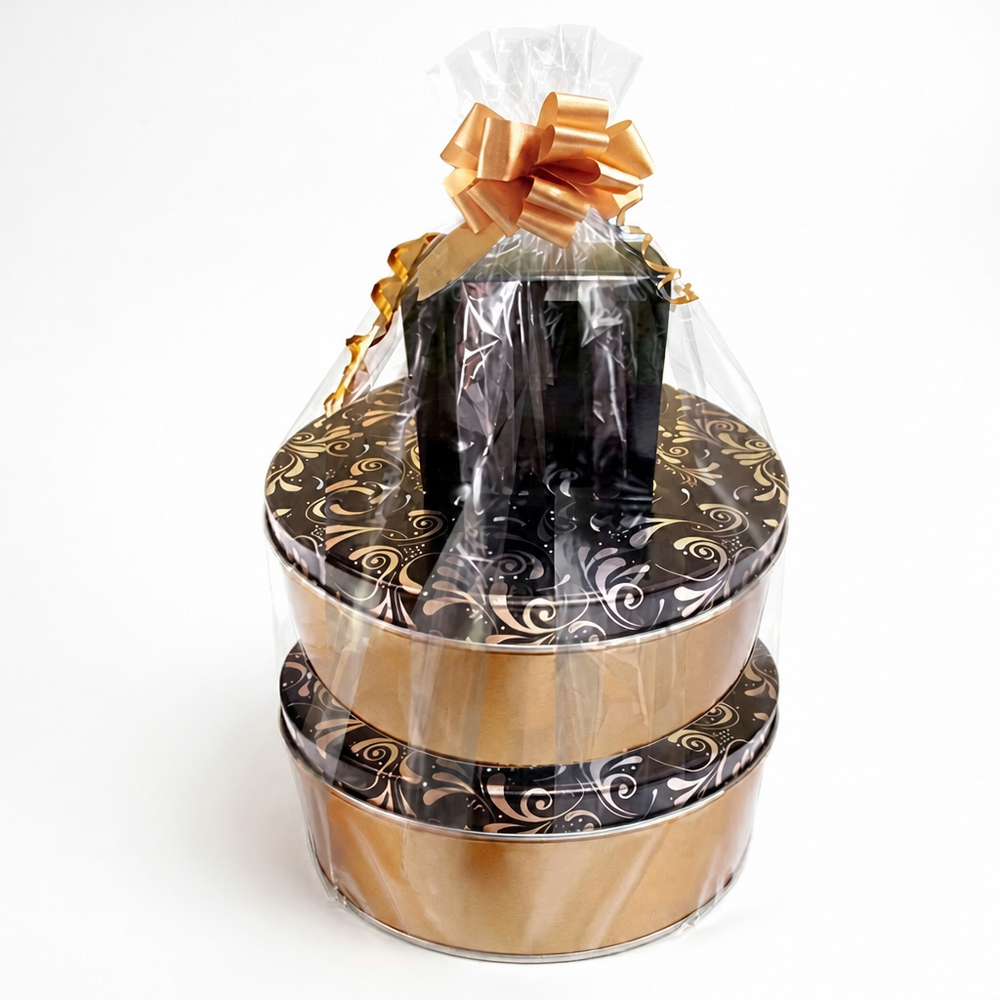 A gift hamper set containing two round black and gold patterned tins stacked vertically, with a smaller black gift box wrapped in clear cellophane and tied with a gold ribbon on top, all photographed against a plain white background.