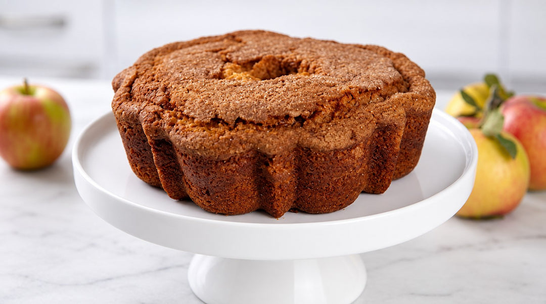 My Grandma's Apple Cider Donut Coffee Cake on a white cake stand, with apples